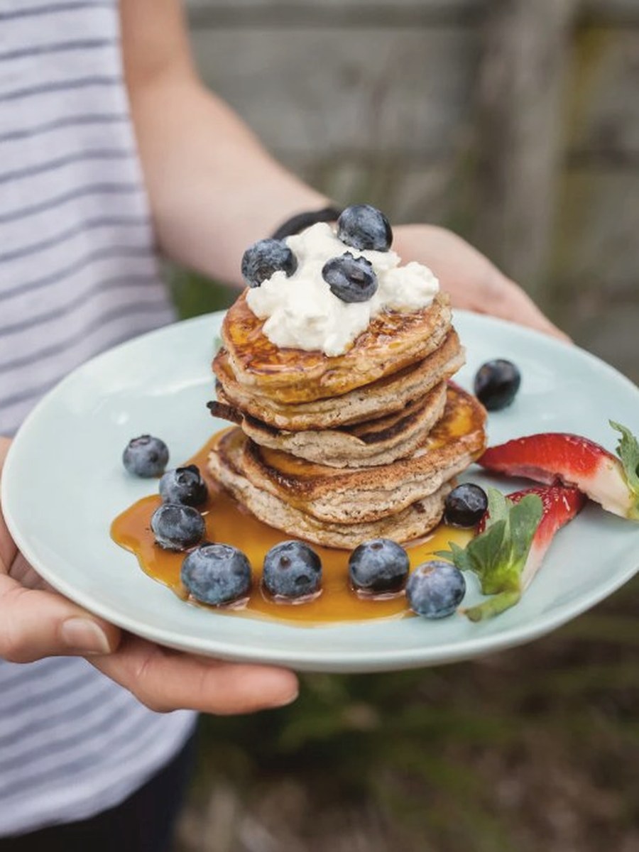 Stack of coconut pancakes topped with blueberries, ricotta and maple syrup