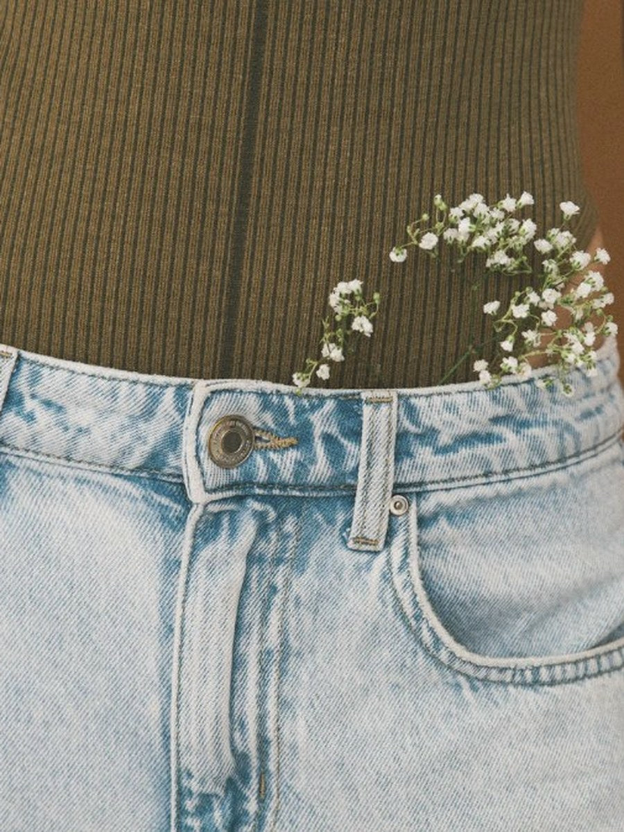 Woman in olive green top and jeans with white baby's breath flowers tucked into her pocket