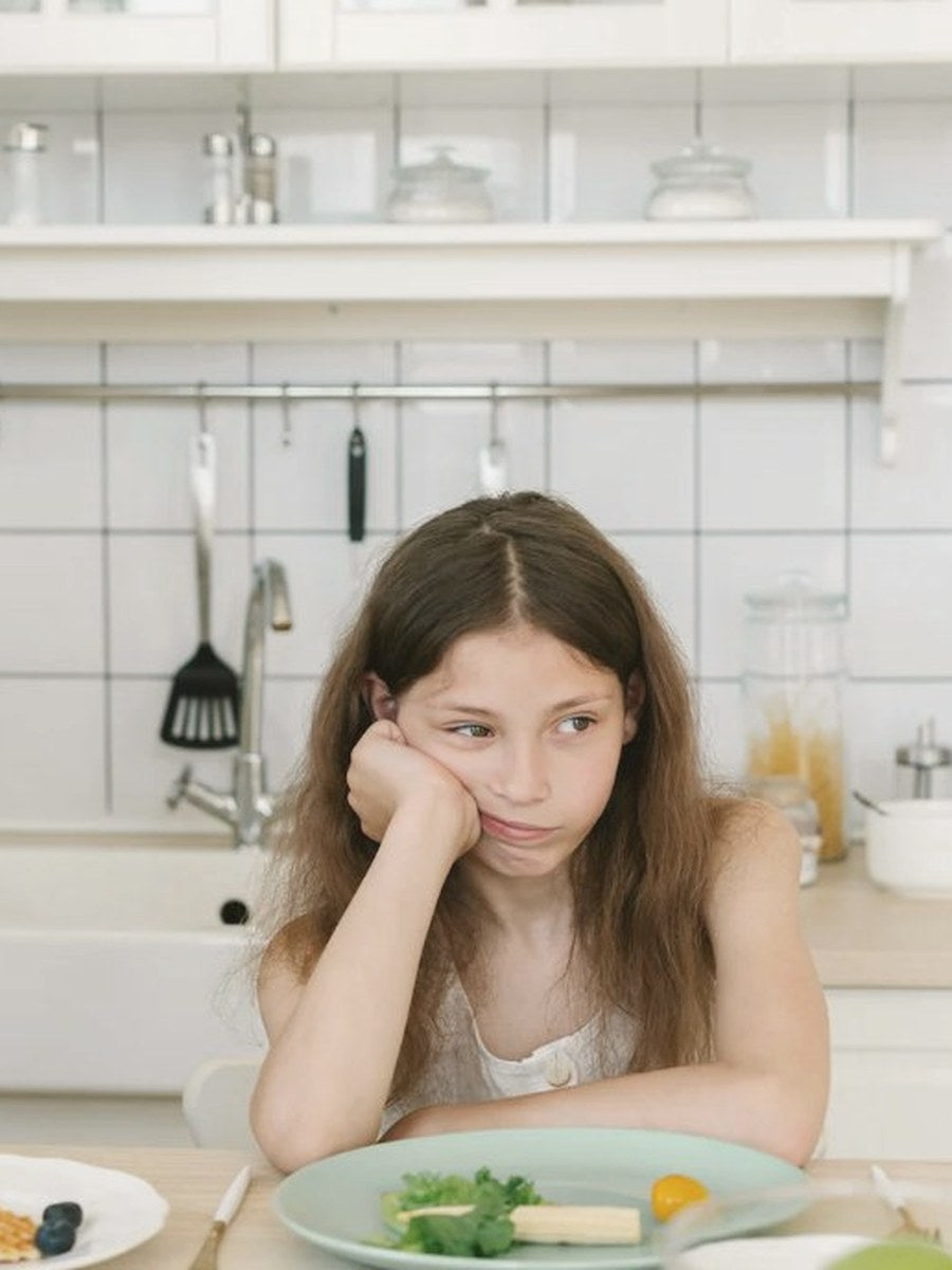 Young girl resting her chin on her hand, looking at a plate of food