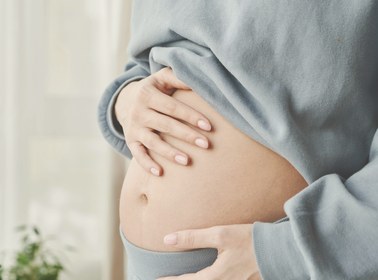 Woman in a soft grey sweatshirt resting both hands gently on her bare midsection