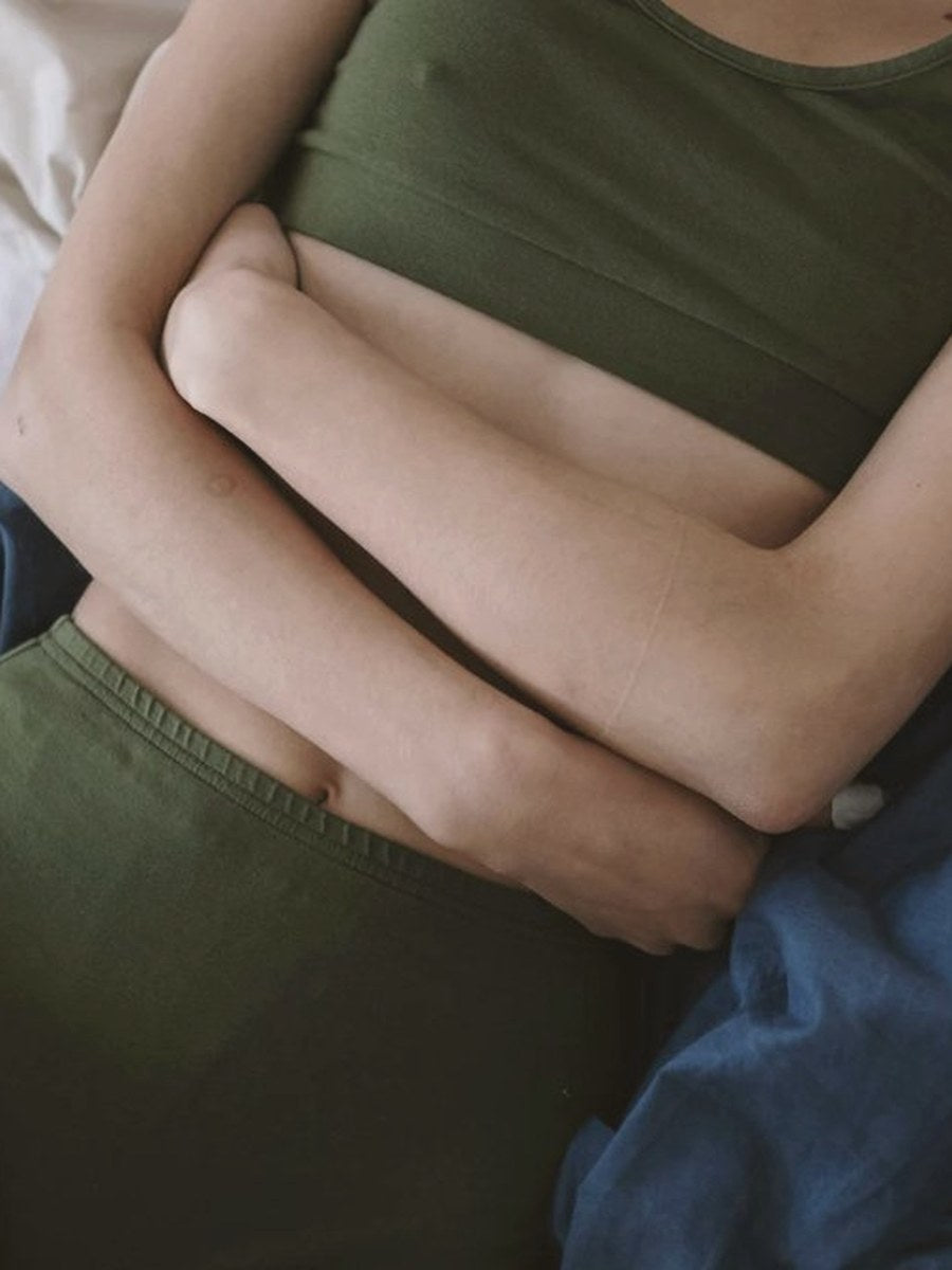 Woman in green crop top and shorts with hands resting on her stomach