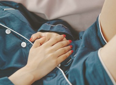 Hands resting clasped over the stomach in navy pyjamas while resting in bed
