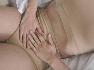 Overhead view of a woman's hands resting gently on her lower abdomen in bed
