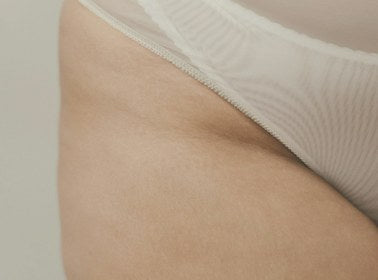 Close-up detail of a woman's hip and thigh in soft white mesh underwear
