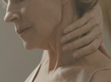 Profile of a mature woman in a peach top, her hand resting at the side of her neck