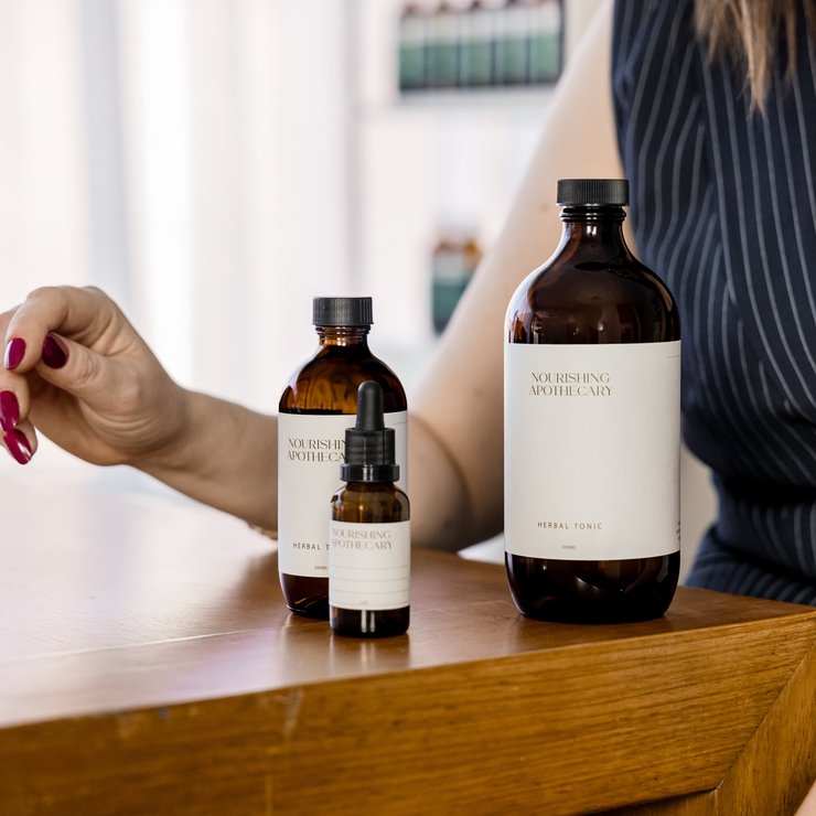 Three bottles of Nourishing Apothecary products on a wooden surface with a blurred background.