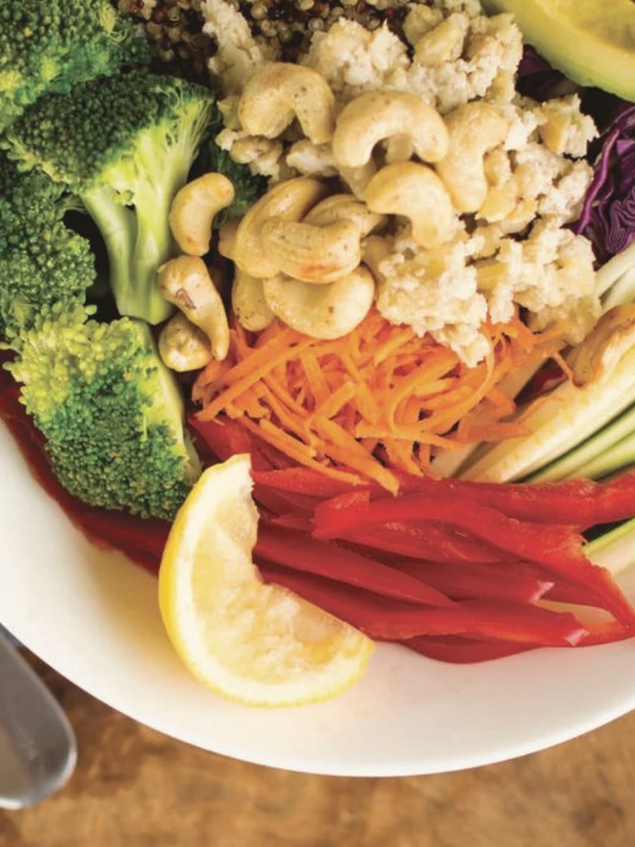 Buddha bowl with broccoli, cashews, carrot, red capsicum, avocado and lemon on a wooden board
