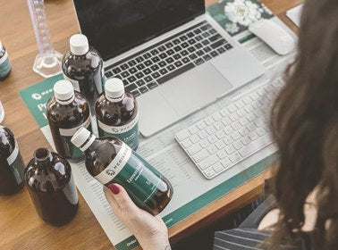 Naturopath holding a herbal tonic bottle while reviewing notes at her clinic desk