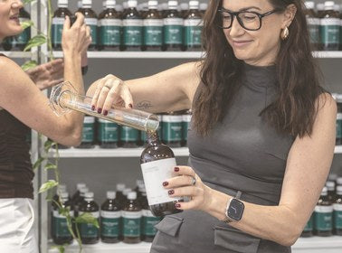 Naturopath pouring a herbal tonic into an amber Nourishing Apothecary bottle in the clinic